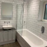 Grey fitted bathroom furniture, sit on basin bowel with LED mirror above. Acrylic bath. Concealed shower vale in bathroom wall. Metro tiles on bathroom walls
