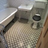 Patterned green bathroom floor tile. Traditional toilet, basin with leg stand, freestanding bath with metro brick tiles on bathroom walls