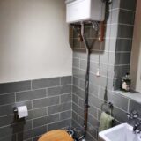 high levelled traditional cistern with pull chain and oak seat. Grey brick tiles on bathroom walls