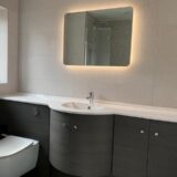 Grey effect fitted furniture with LED mirror above and floating toilet within unit